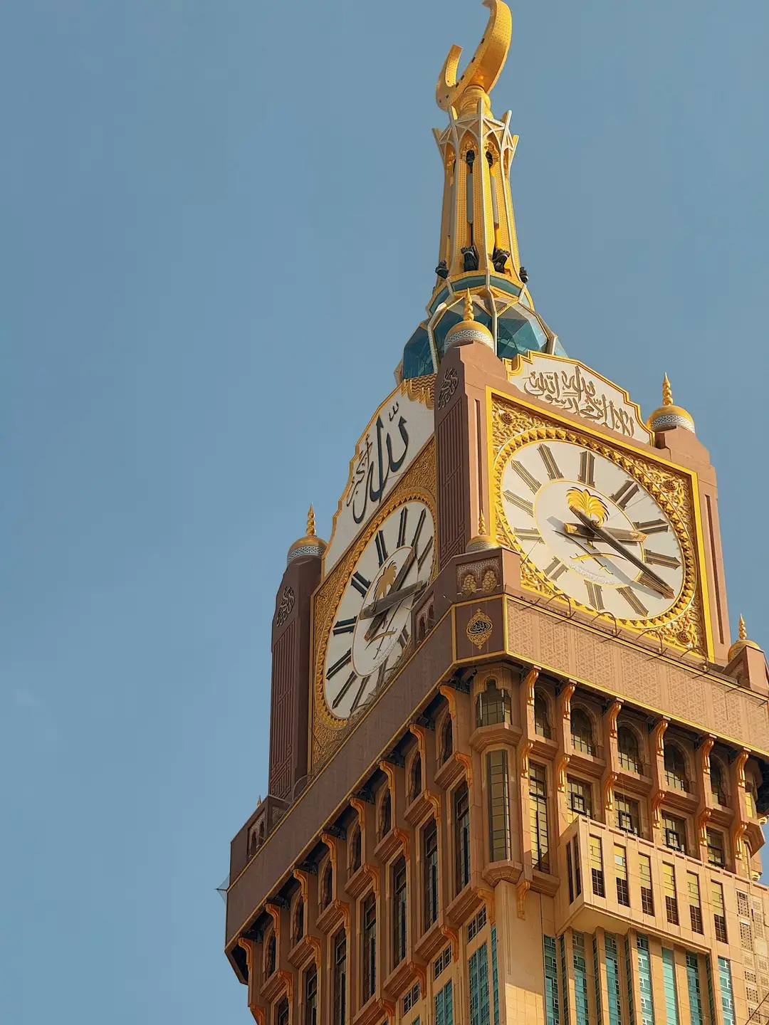 The crescent at the top of the Makkah clock tower against a pale blue sky