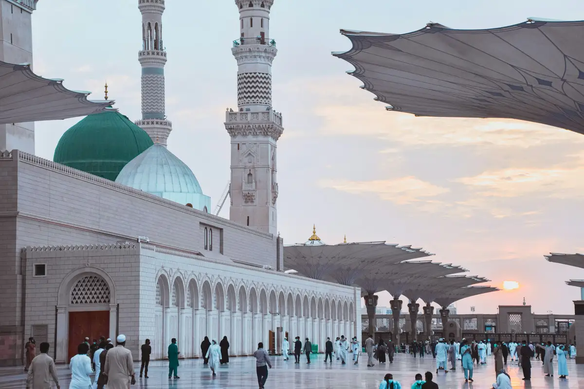 The Green Dome and minarets of the Prophet's Mosque at dusk, framed by the shade umbrellas