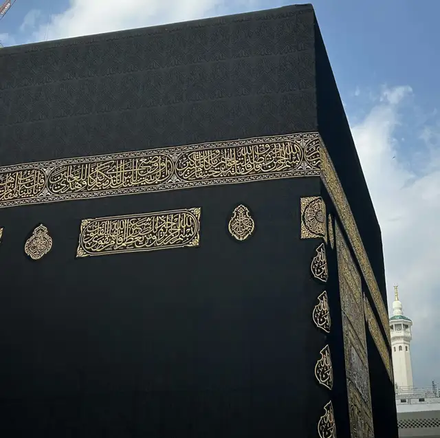 The corner of the Kaaba, its gold-embroidered Kiswah against a clear sky