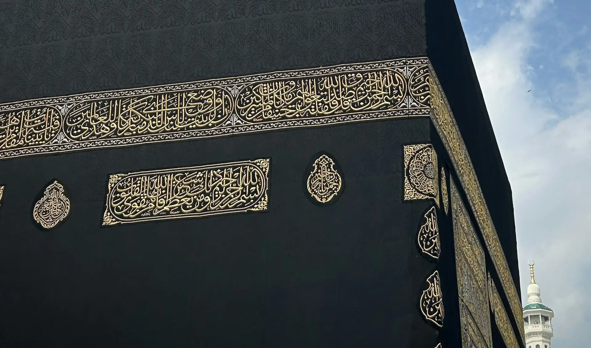 The corner of the Kaaba, its gold-embroidered Kiswah against a clear sky