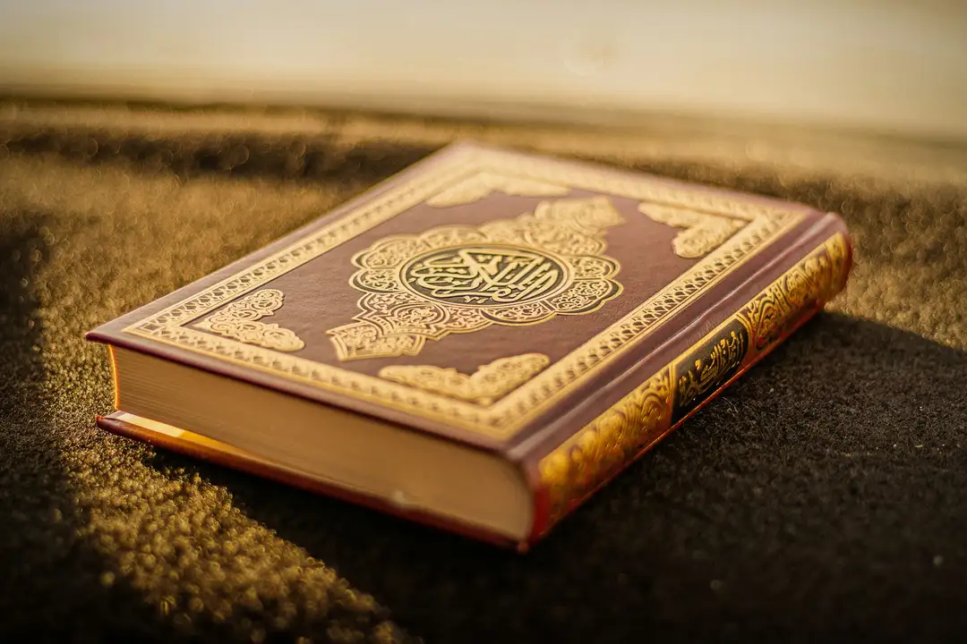 A gold-embossed Quran resting on a prayer mat in warm light