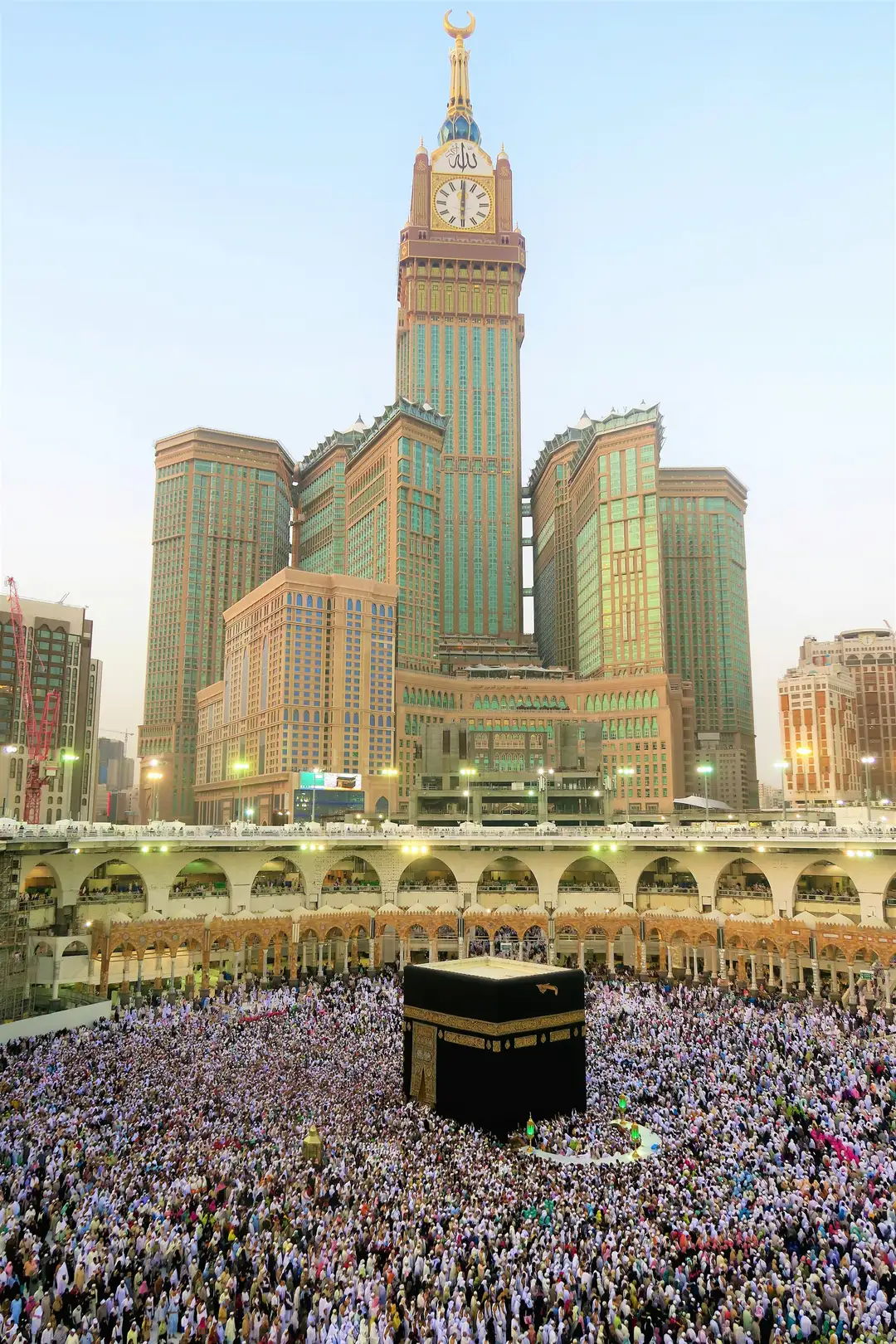 The Kaaba below the Makkah clock tower, surrounded by a crowded courtyard