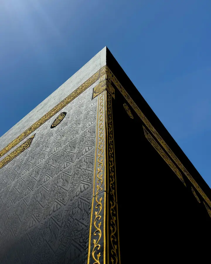 The corner of the Kaaba seen from below, its gold-embroidered Kiswah against a deep blue sky
