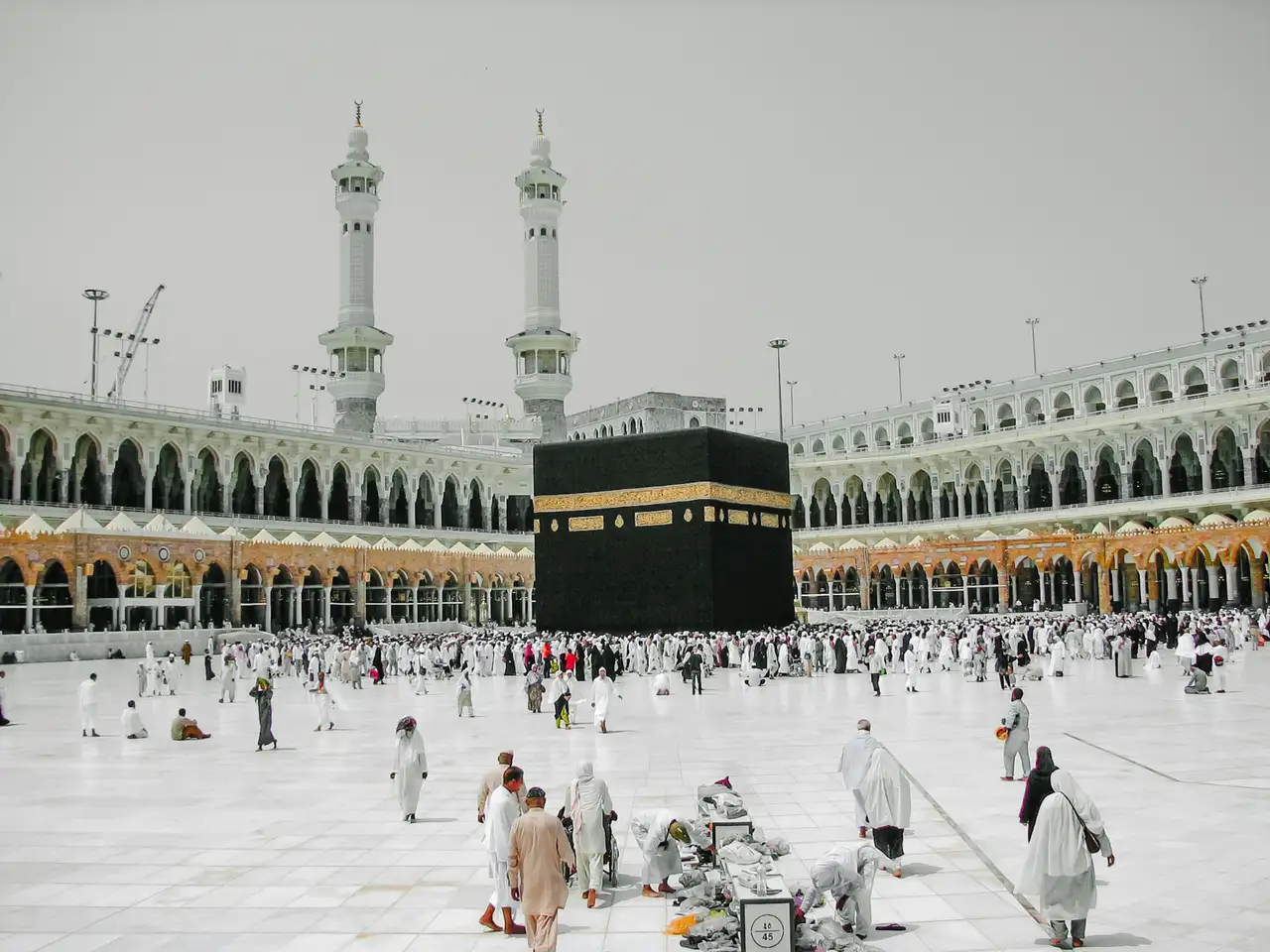 Pilgrims in white ihram walking around the Kaaba under a clear blue sky