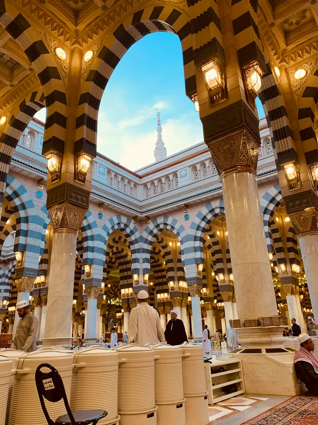 Worshippers seated beneath striped arches and brass lanterns in the Prophet's Mosque