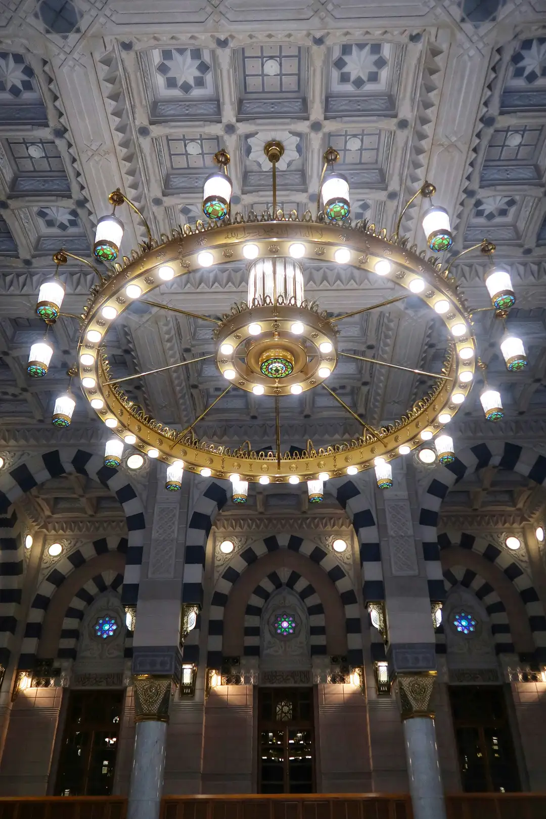 A brass chandelier hanging beneath the painted domes of the Prophet's Mosque in Madinah