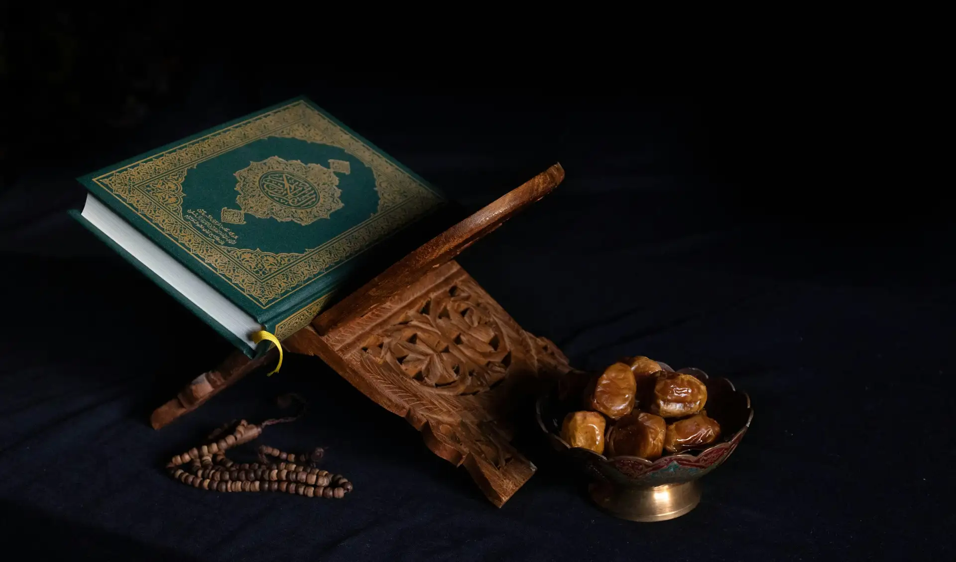 A Quran on a carved stand beside dates and prayer beads