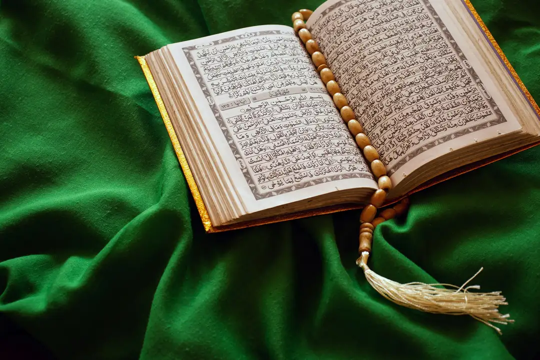 An open Quran with prayer beads resting on green fabric