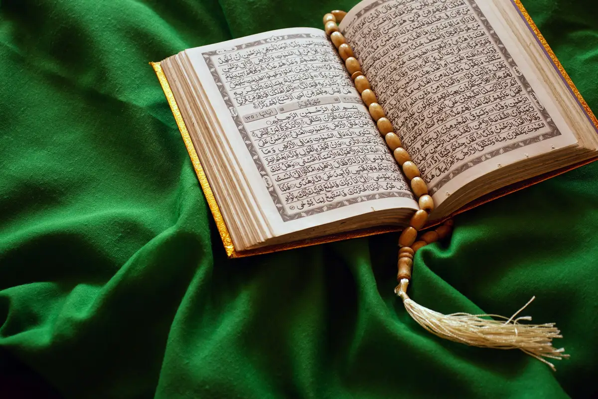 An open Quran with prayer beads resting on green fabric