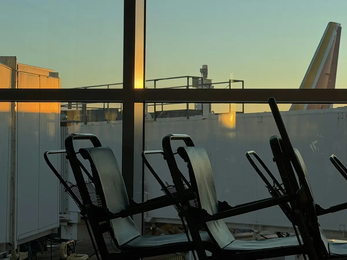 An airport terminal window at sunset with a plane tail beyond the jet bridges